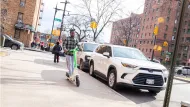 Person riding electric scooter on New York City sidewalk.